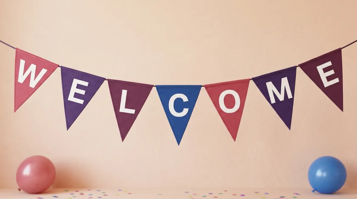 A string of pennant flags that spell WELCOME on a peach wall, with a pink and a blue balloon below.