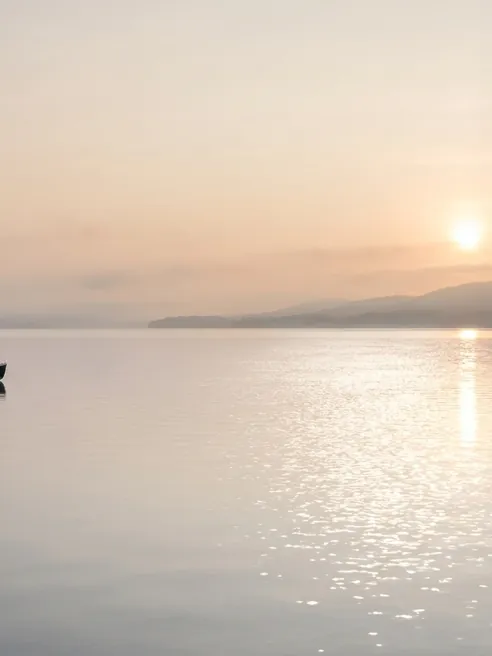 The lake, the hills and the sun are left, but the boat at the left edge is cut away.