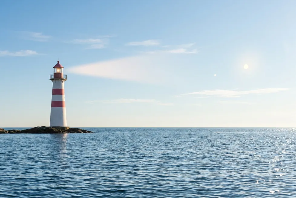 A red and white lighthouse on a small rocky island in a calm blue sea, under a clear sky.